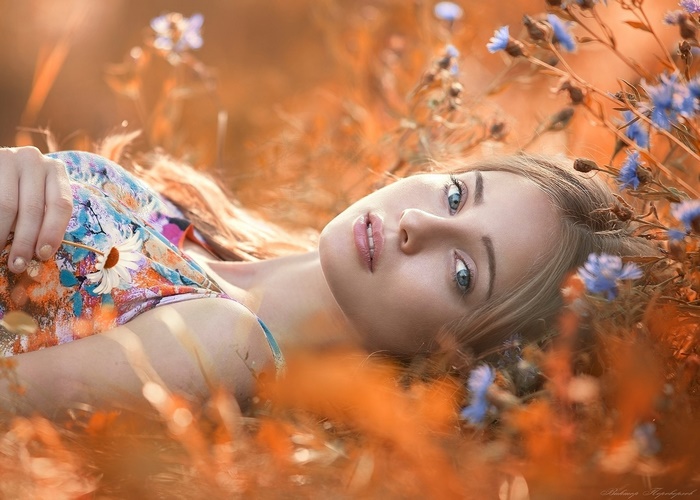 Woman with blonde hair and blue eyes lying in a field