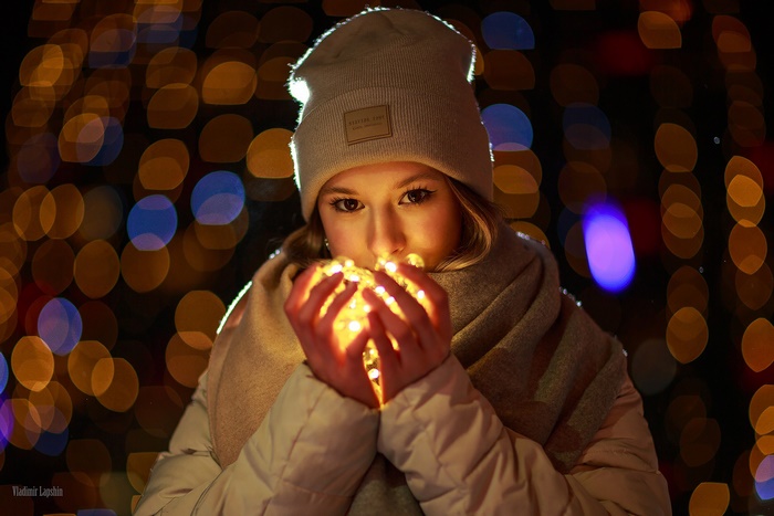 Woman in beanie holding glowing string lights