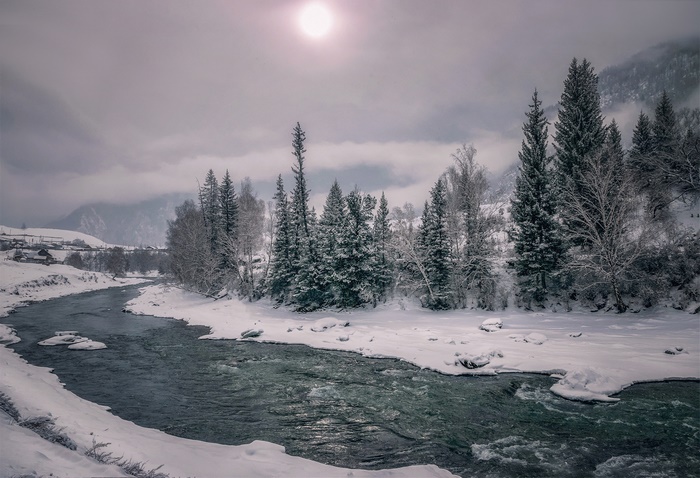River in a snowy landscape with trees and mountains