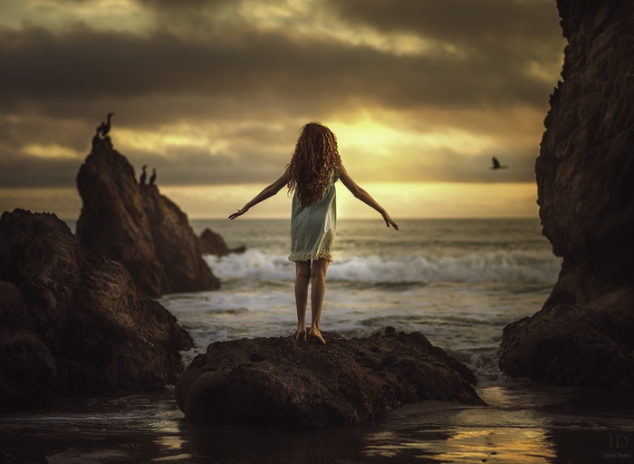 Girl with red hair on rocks at sunset