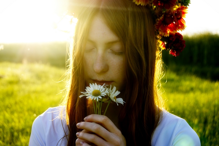 Woman with flower crown smelling daisies in sunlight