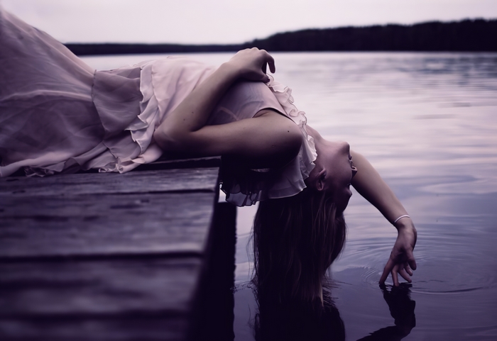 Woman in pink dress lying on a dock touching water