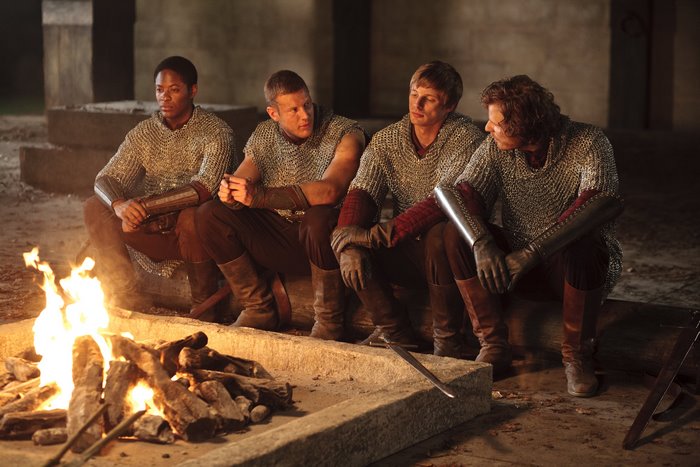 Four Knights from Merlin sitting by a campfire
