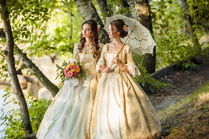 Two women in historical dresses with parasol and bouquet