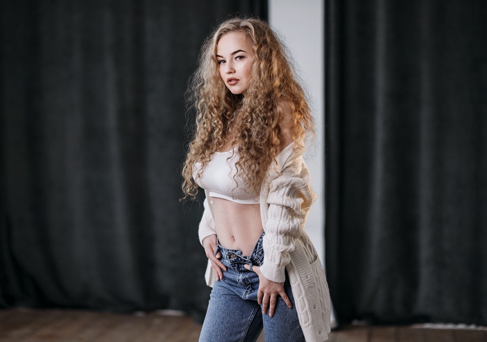 Woman with long curly hair wearing a white top and jeans