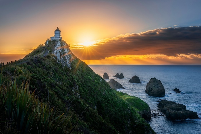 Lighthouse on a hill at sunrise with ocean and rocks