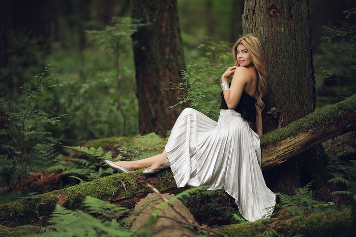 Woman in skirt sitting on a log in a forest