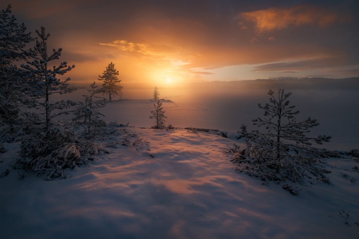 Snowy landscape with sunrise over a foggy lake