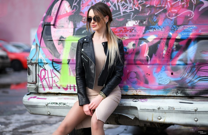 Woman in leather jacket and sunglasses sitting by graffiti van