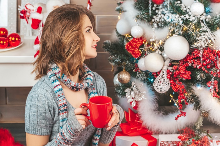 Woman holding a red mug near a Christmas tree