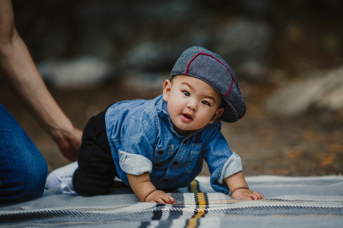 Baby boy in denim shirt and cap crawling on blanket