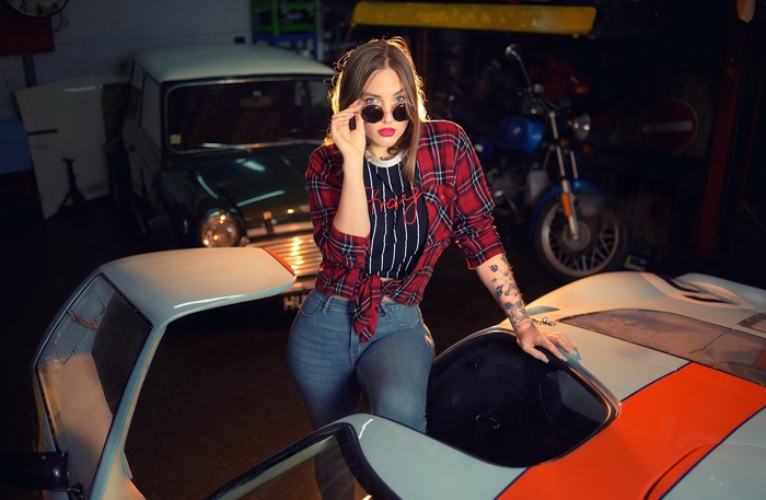 Woman with sunglasses and tattoos leaning on a sports car