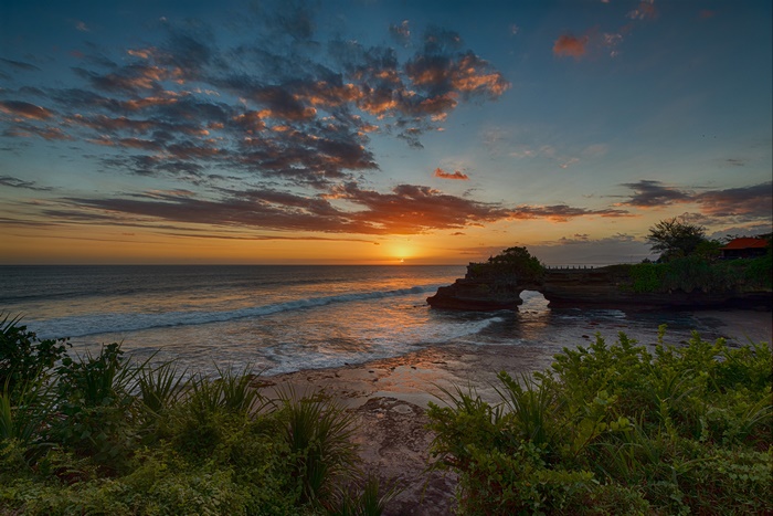 Sunset over the ocean with rock arch and clouds