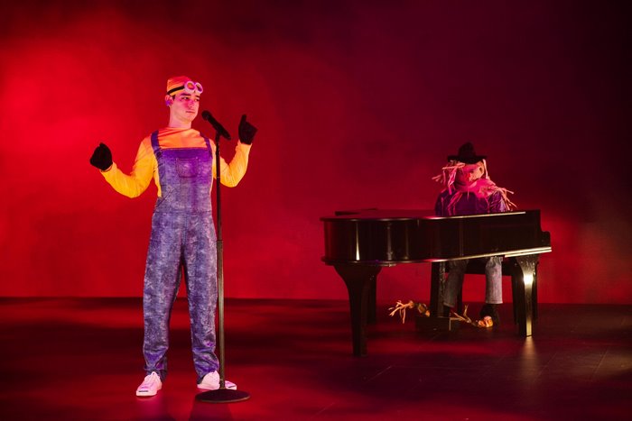 Performer in Minion costume singing on stage with scarecrow at piano