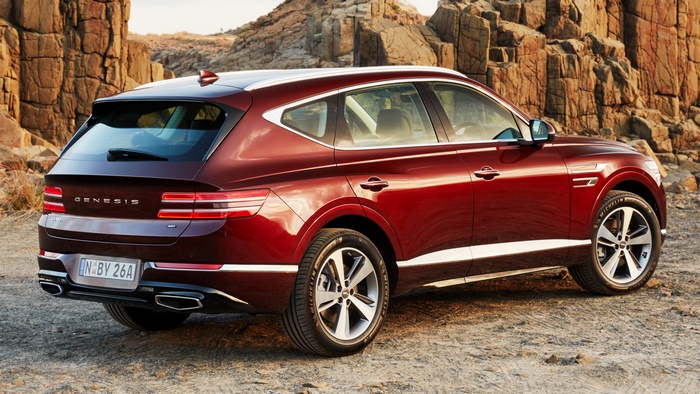 Red Genesis GV80 SUV parked on dirt road with rocky hills