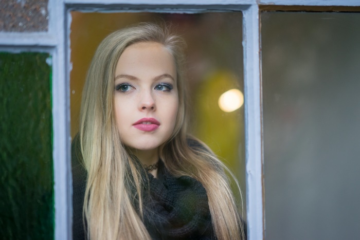 Woman with blonde hair and blue eyes looking out a window