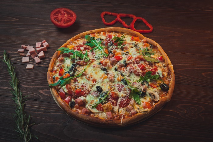 Pizza with ham, olives, and vegetables on a wooden table