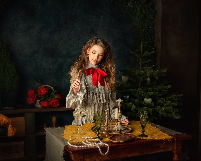 Girl in vintage dress with red bow by Christmas tree