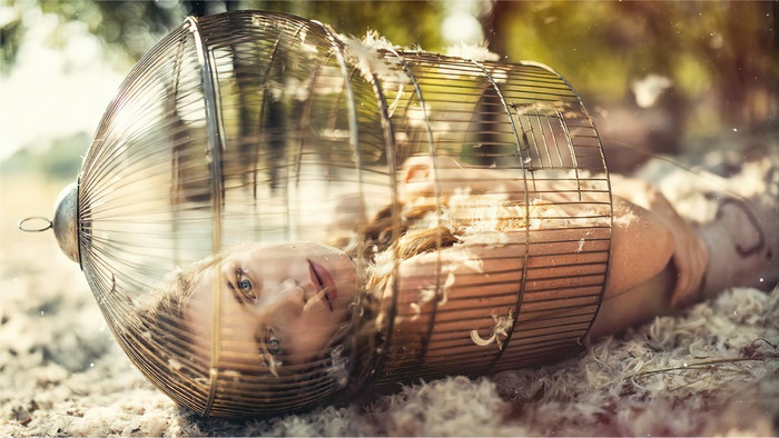 Woman in a birdcage with feathers outdoors