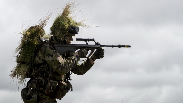 Soldier with camouflage and foliage aiming a rifle