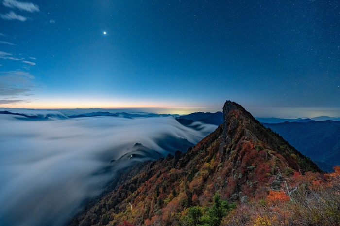 Mountain peak with fog and stars at night