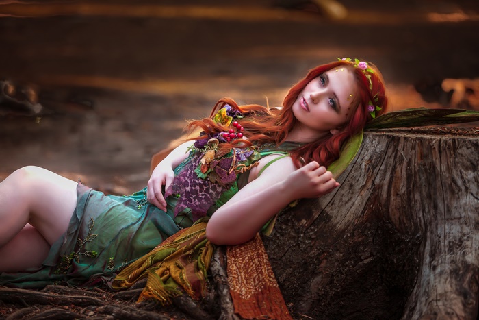 Redhead woman in a green dress lying on a tree stump