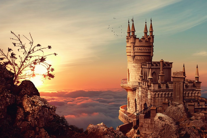 Castle on a cliff above clouds at sunset