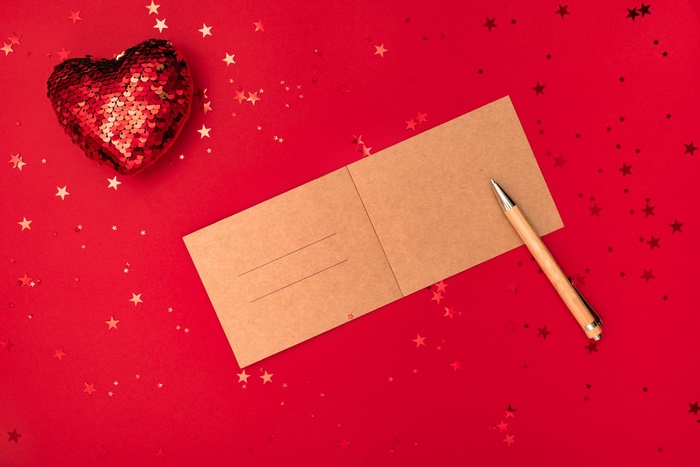 Red sequin heart, postcard, and pen on red background