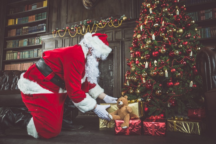 Santa Claus placing gifts under a Christmas tree