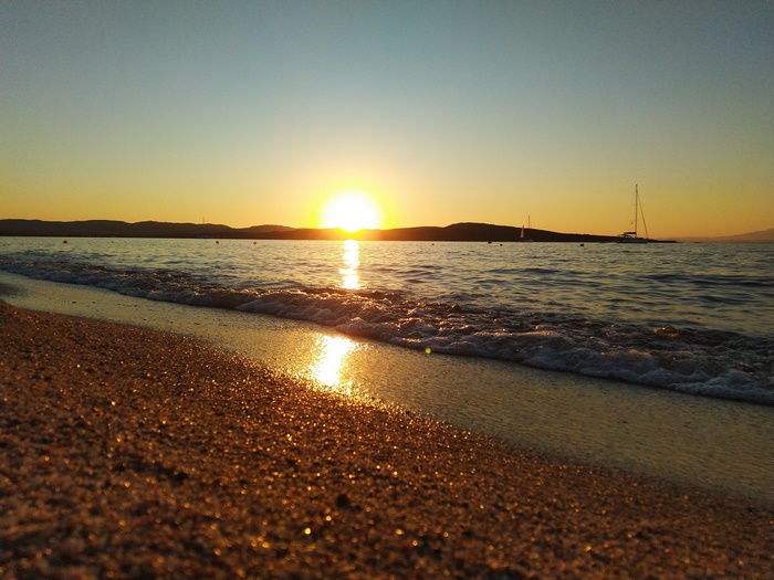 Sunset over the sea with a beach and sailboat