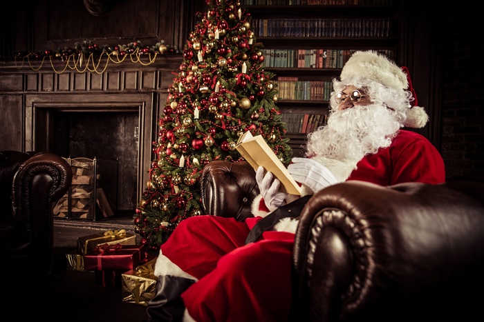 Santa Claus reading a book by the Christmas tree