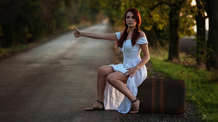 Redhead woman hitchhiking in white dress with suitcase