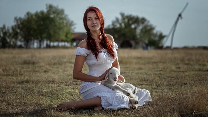 Woman in white dress holding a lamb in a meadow