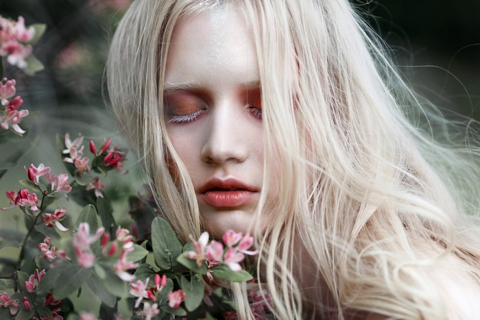 Model with blonde hair and makeup near flowers