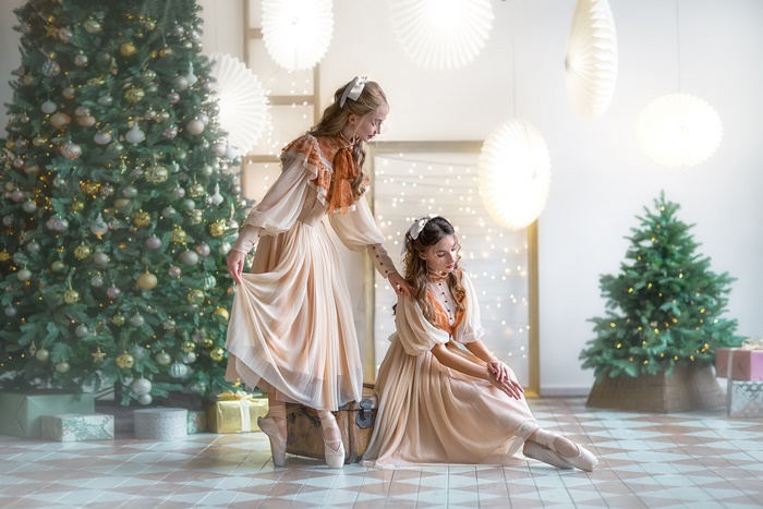 Two ballerinas in vintage dresses by a Christmas tree