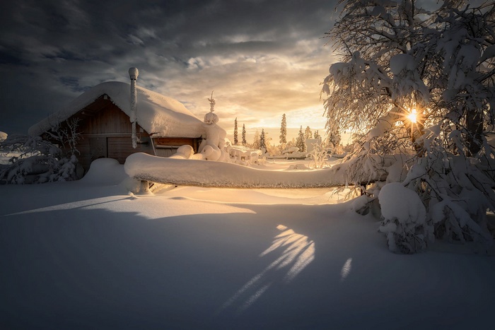 Snowy cabin with sunbeams through trees