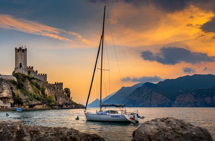 Castle on a cliff overlooking a lake with a sailboat at sunset