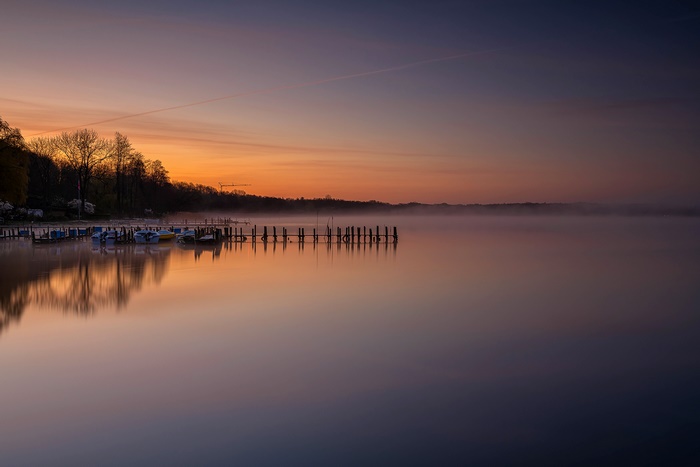Boats docked at a pier on a misty lake at sunrise