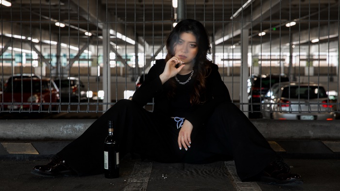 Woman smoking cigarette with bottle in parking lot