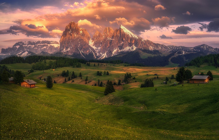 Alps mountain range with huts and meadows at sunset