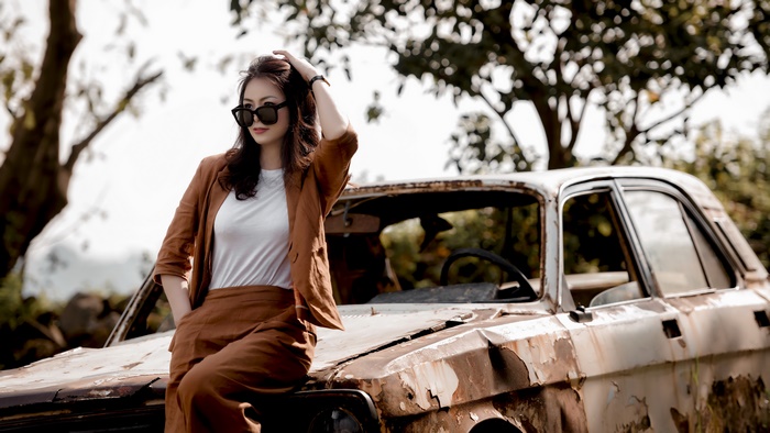 Woman with sunglasses posing near a rusty car