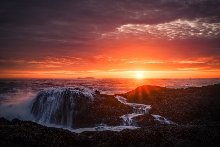Sunset over ocean with waterfall on rocks