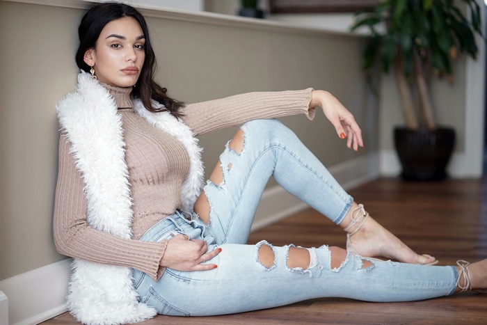 Woman with black hair wearing ripped jeans and a fur vest