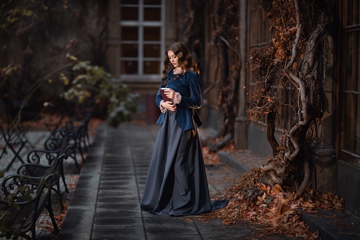 Woman in vintage dress holding a book in autumn courtyard