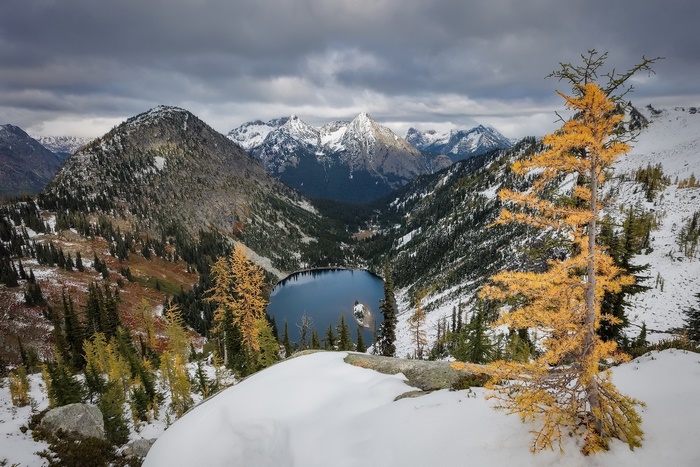 Lake in a mountain valley with autumn trees and snow