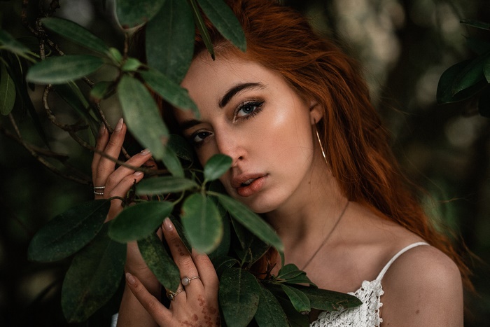 Redhead woman peeking through green leaves