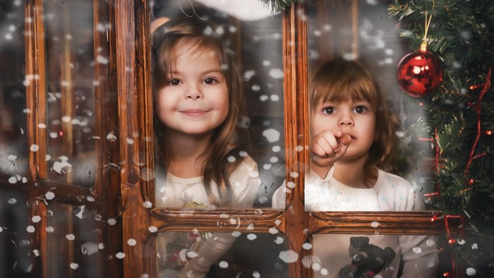 Two young girls looking out a window at Christmas