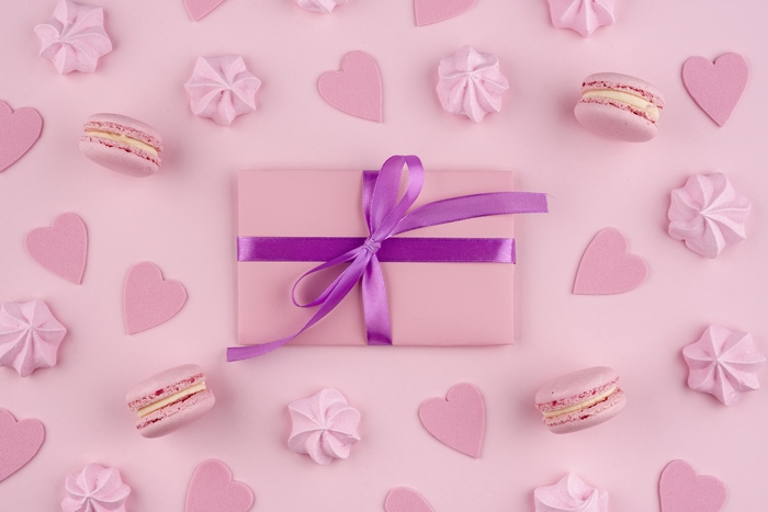 Pink gift with purple ribbon surrounded by macarons and meringues