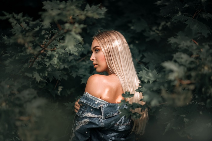 Blonde woman in denim jacket among green leaves