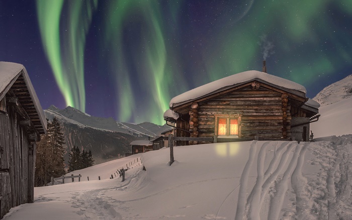 Log cabin under Aurora Borealis in snowy mountains